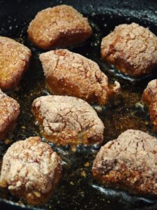 Close-up of crispy fried chicken pieces cooking in hot oil.
