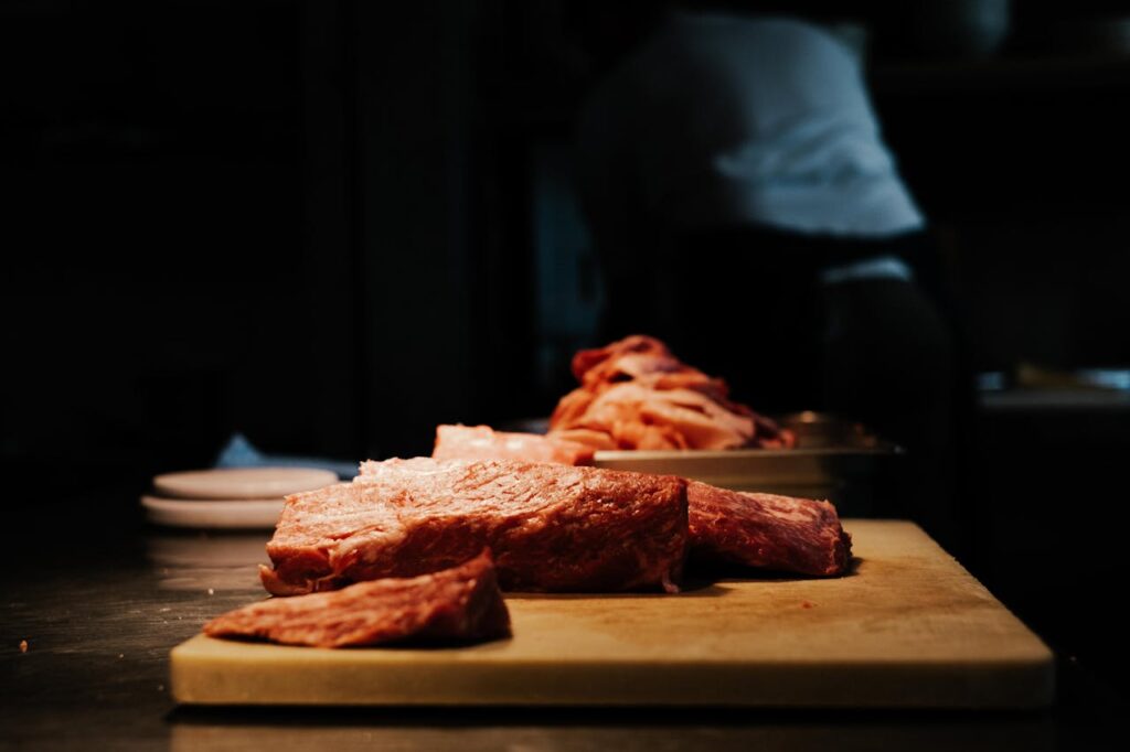 Slices of raw meat on a wooden cutting board in a dimly lit kitchen setting.